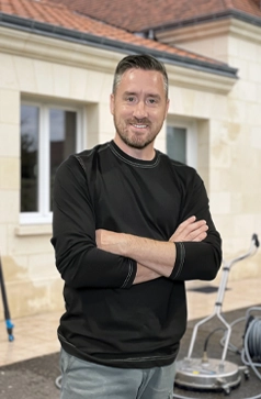 Cédric Caudal, fondateur d'Eauxigen, devant une maison en tuffeau fraîchement nettoyée en Val de Loire, avec son matériel de nettoyage softwash — perche télescopique et nettoyeur de surface rotatif, devis gratuit sous 24h